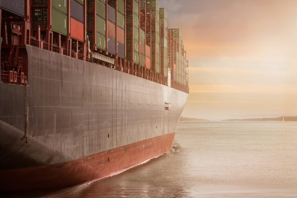 pexels-photo-262353-262353 A colossal cargo ship loaded with containers navigates through calm waters against a vibrant sunset sky.